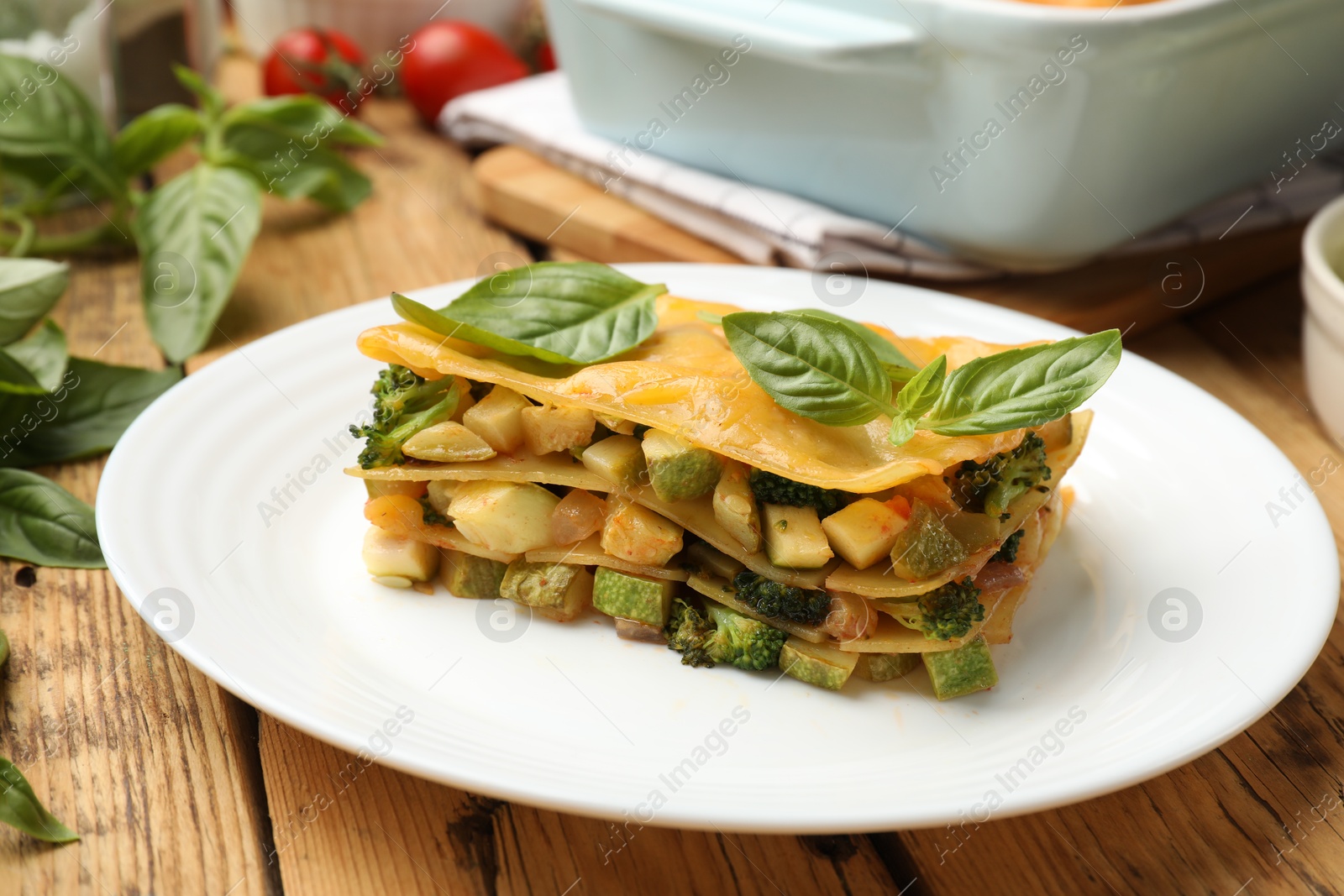 Photo of Piece of tasty vegetarian lasagna and ingredients on wooden table, closeup