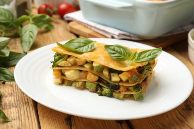 Photo of Piece of tasty vegetarian lasagna and ingredients on wooden table, closeup