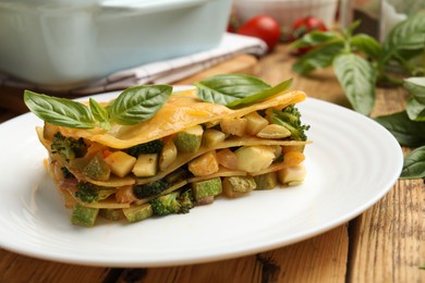 Photo of Piece of tasty vegetarian lasagna and ingredients on wooden table, closeup