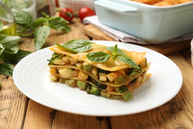 Photo of Piece of tasty vegetarian lasagna and ingredients on wooden table, closeup