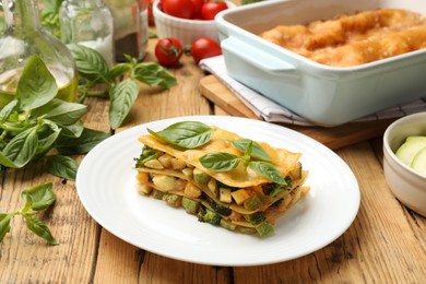 Photo of Piece of tasty vegetarian lasagna and ingredients on wooden table
