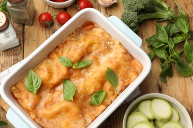 Photo of Tasty vegetarian lasagna in baking dish and ingredients on wooden table, flat lay
