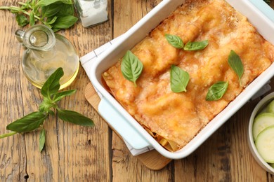 Photo of Tasty vegetarian lasagna in baking dish and ingredients on wooden table, flat lay