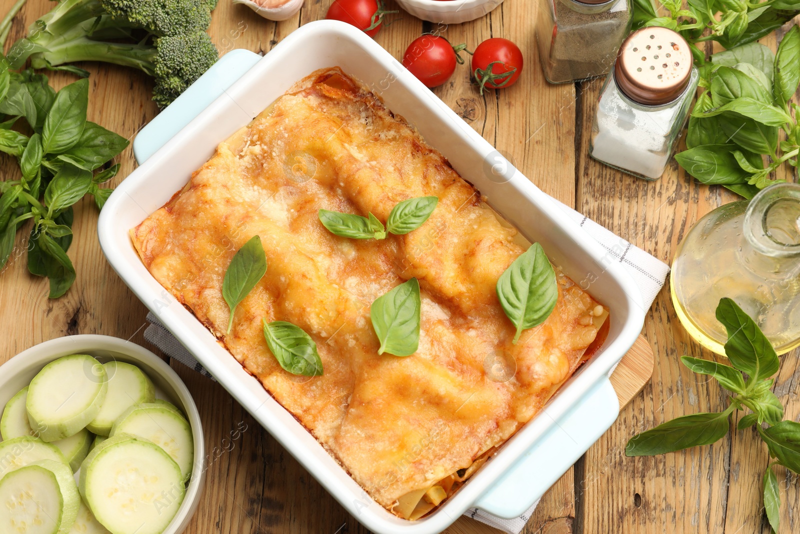 Photo of Tasty vegetarian lasagna in baking dish and ingredients on wooden table, flat lay