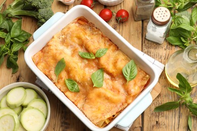 Photo of Tasty vegetarian lasagna in baking dish and ingredients on wooden table, flat lay