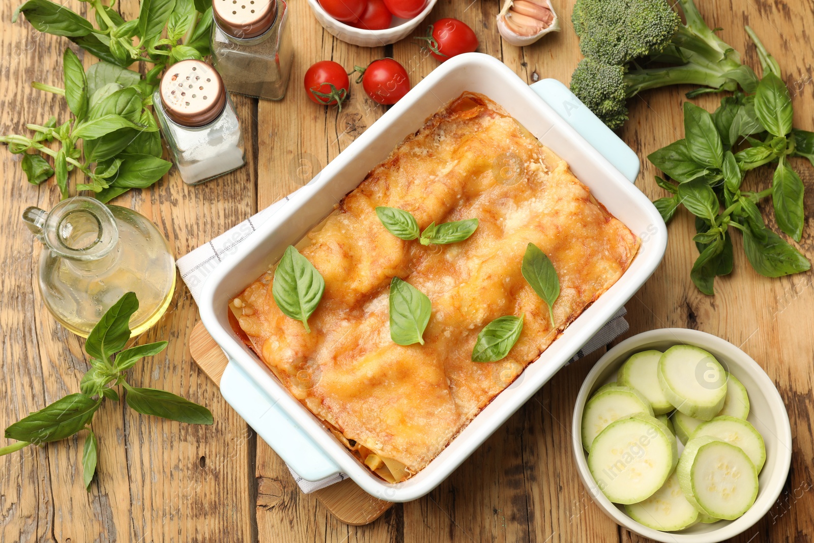 Photo of Tasty vegetarian lasagna in baking dish and ingredients on wooden table, flat lay