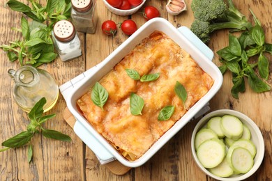 Photo of Tasty vegetarian lasagna in baking dish and ingredients on wooden table, flat lay