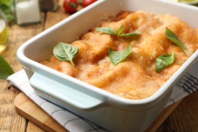 Photo of Tasty vegetarian lasagna in baking dish and ingredients on wooden table, closeup