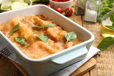 Photo of Tasty vegetarian lasagna in baking dish and ingredients on wooden table, closeup