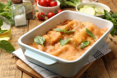 Photo of Tasty vegetarian lasagna in baking dish and ingredients on wooden table, closeup