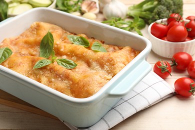 Photo of Tasty vegetarian lasagna in baking dish and ingredients on white wooden table, closeup