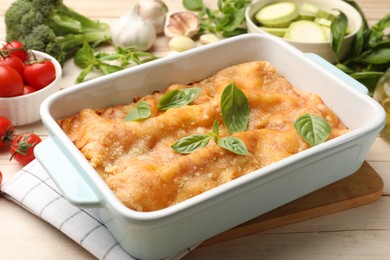Photo of Tasty vegetarian lasagna in baking dish and ingredients on white wooden table, closeup