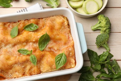 Photo of Tasty vegetarian lasagna in baking dish and ingredients on white wooden table, flat lay
