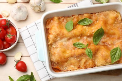 Photo of Tasty vegetarian lasagna in baking dish and ingredients on white wooden table, flat lay