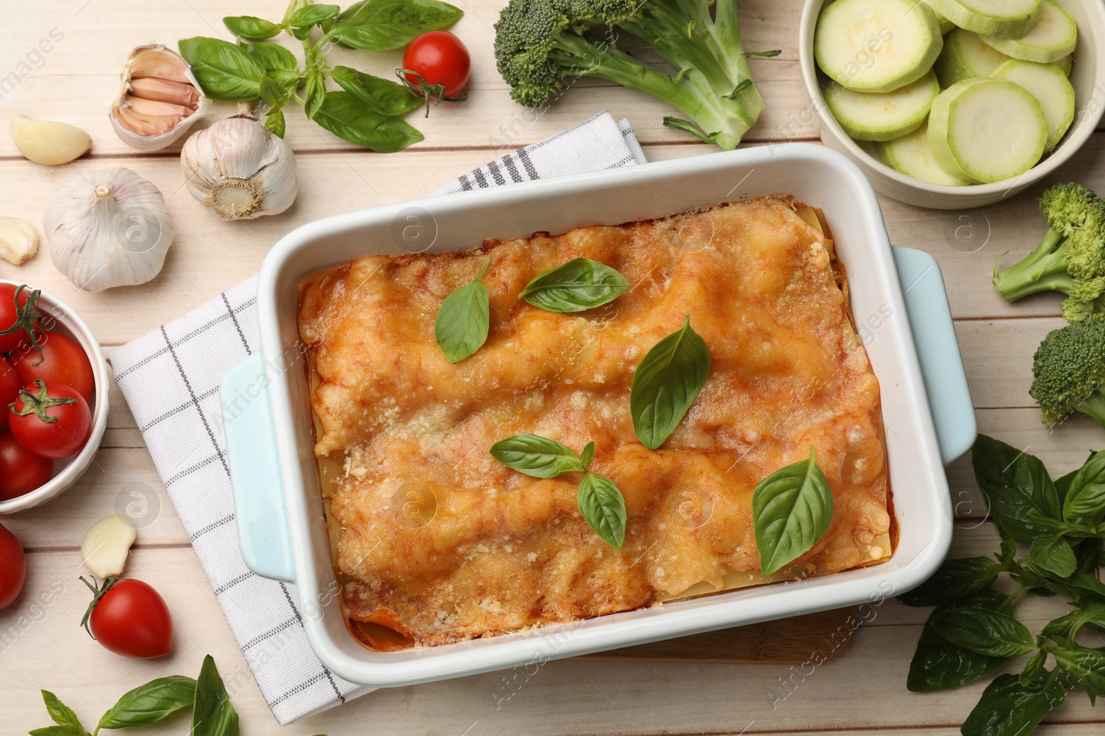 Tasty vegetarian lasagna in baking dish and ingredients on white wooden table, flat lay Photo of Tasty vegetarian lasagna in baking dish and ingredients on white wooden table, flat lay