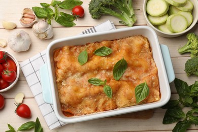 Photo of Tasty vegetarian lasagna in baking dish and ingredients on white wooden table, flat lay