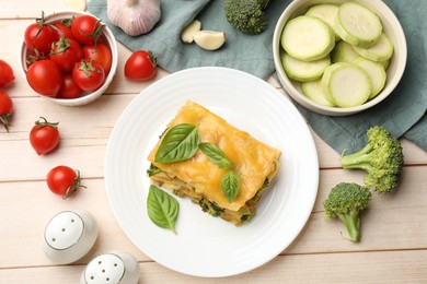 Photo of Piece of tasty vegetarian lasagna and ingredients on white wooden table, flat lay