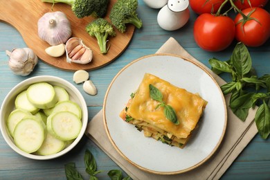 Photo of Piece of tasty vegetarian lasagna and ingredients on blue wooden table, flat lay