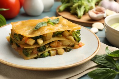 Photo of Piece of tasty vegetarian lasagna and ingredients on blue wooden table, closeup