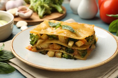 Photo of Piece of tasty vegetarian lasagna and ingredients on blue wooden table, closeup