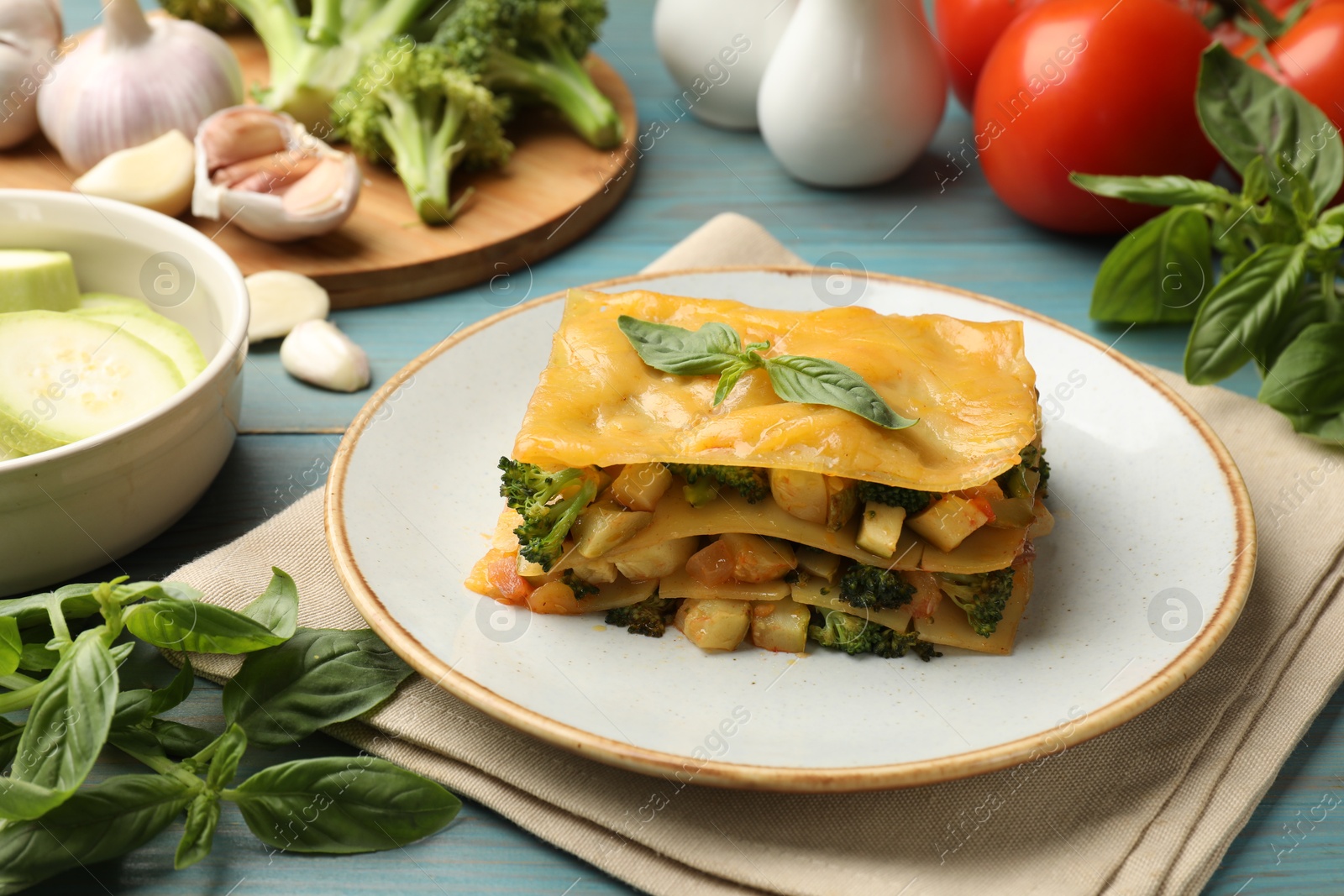 Piece of tasty vegetarian lasagna and ingredients on blue wooden table, closeup Photo of Piece of tasty vegetarian lasagna and ingredients on blue wooden table, closeup