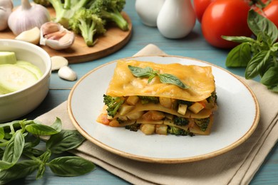 Photo of Piece of tasty vegetarian lasagna and ingredients on blue wooden table, closeup
