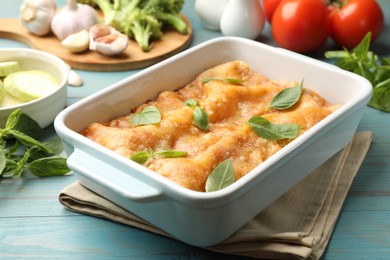 Photo of Tasty vegetarian lasagna in baking dish and ingredients on blue wooden table, closeup