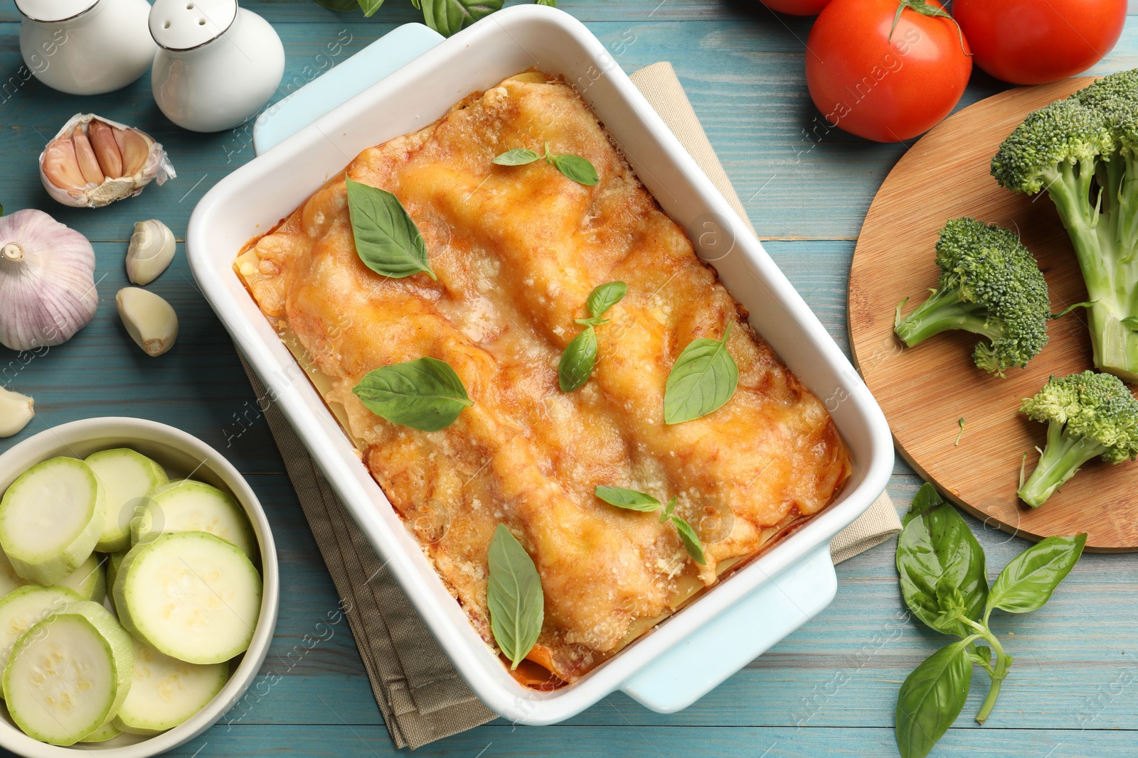 Tasty vegetarian lasagna in baking dish and ingredients on blue wooden table, flat lay Photo of Tasty vegetarian lasagna in baking dish and ingredients on blue wooden table, flat lay