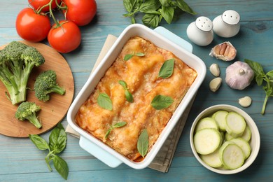 Photo of Tasty vegetarian lasagna in baking dish and ingredients on blue wooden table, flat lay