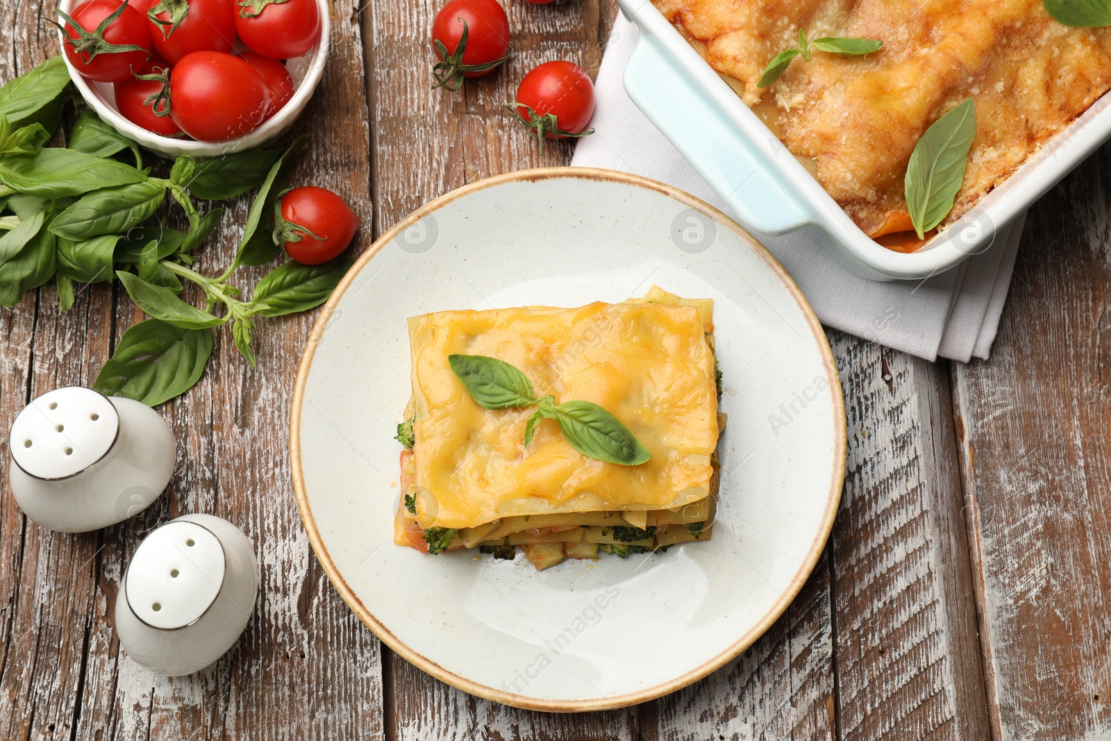 Photo of Piece of tasty vegetarian lasagna and ingredients on wooden table, flat lay