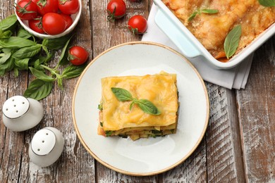 Photo of Piece of tasty vegetarian lasagna and ingredients on wooden table, flat lay