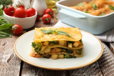 Photo of Piece of tasty vegetarian lasagna and ingredients on wooden table, closeup