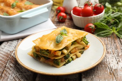 Photo of Piece of tasty vegetarian lasagna and ingredients on wooden table, closeup