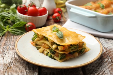 Photo of Piece of tasty vegetarian lasagna and ingredients on wooden table, closeup