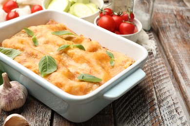 Photo of Tasty vegetarian lasagna in baking dish and ingredients on wooden table, closeup