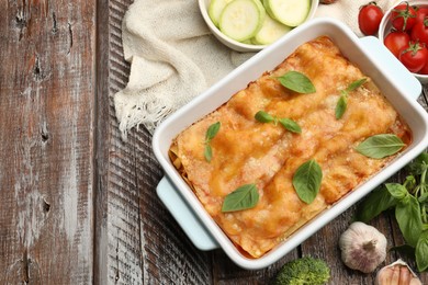 Photo of Tasty vegetarian lasagna in baking dish and ingredients on wooden table, flat lay. Space for text