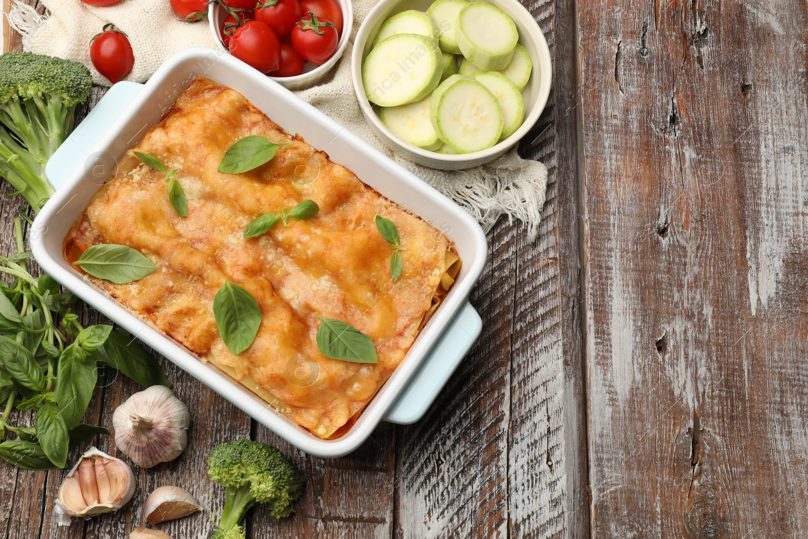 Tasty vegetarian lasagna in baking dish and ingredients on wooden table, flat lay. Space for text Photo of Tasty vegetarian lasagna in baking dish and ingredients on wooden table, flat lay. Space for text