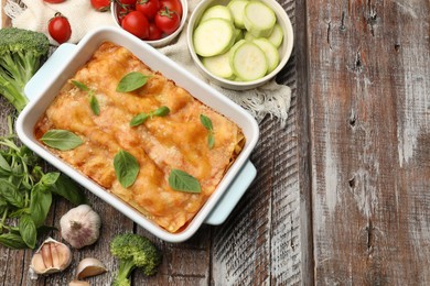 Photo of Tasty vegetarian lasagna in baking dish and ingredients on wooden table, flat lay. Space for text