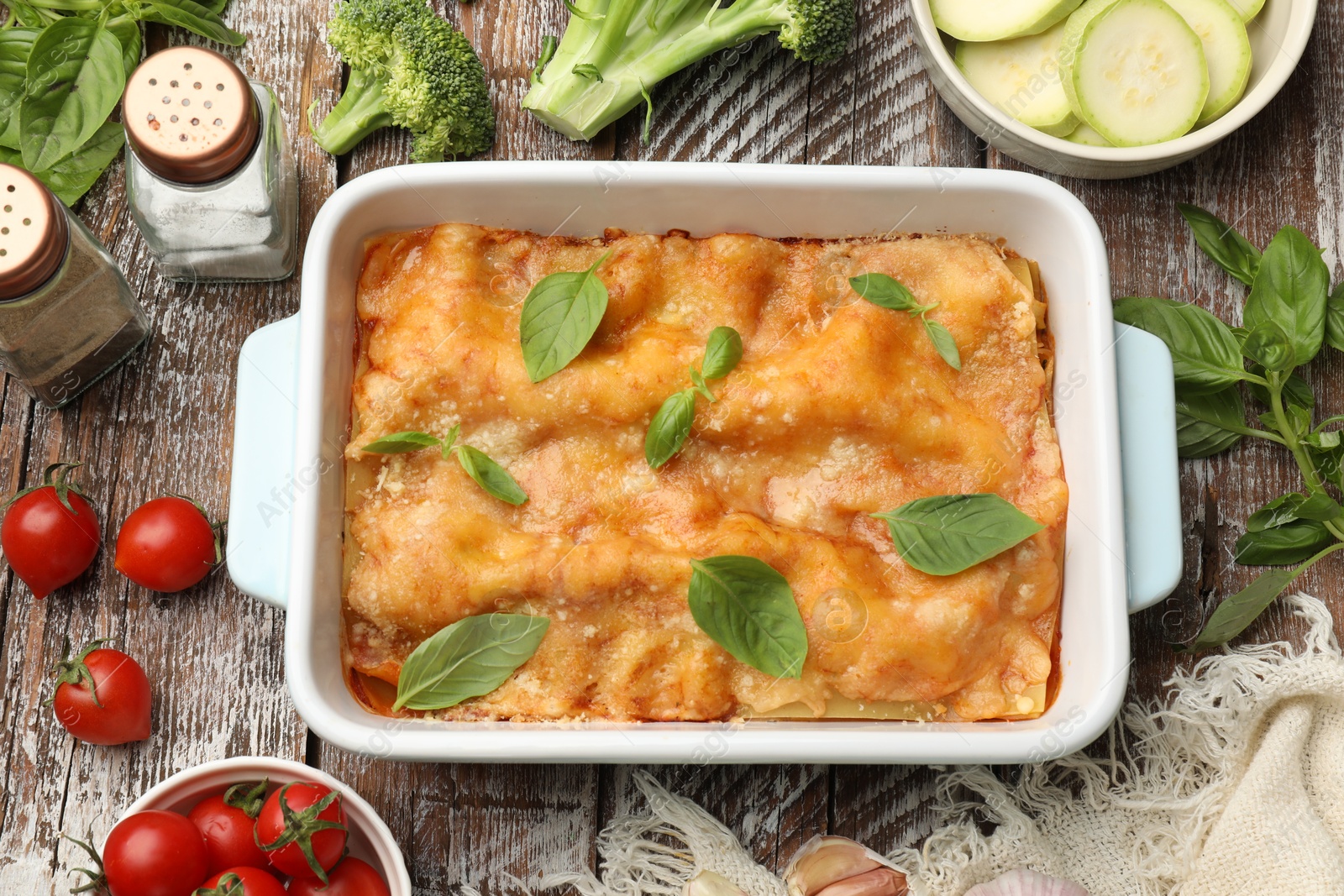 Tasty vegetarian lasagna in baking dish and ingredients on wooden table, flat lay Photo of Tasty vegetarian lasagna in baking dish and ingredients on wooden table, flat lay