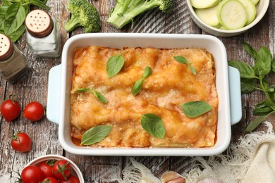 Photo of Tasty vegetarian lasagna in baking dish and ingredients on wooden table, flat lay