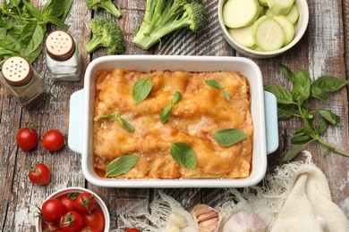 Photo of Tasty vegetarian lasagna in baking dish and ingredients on wooden table, flat lay