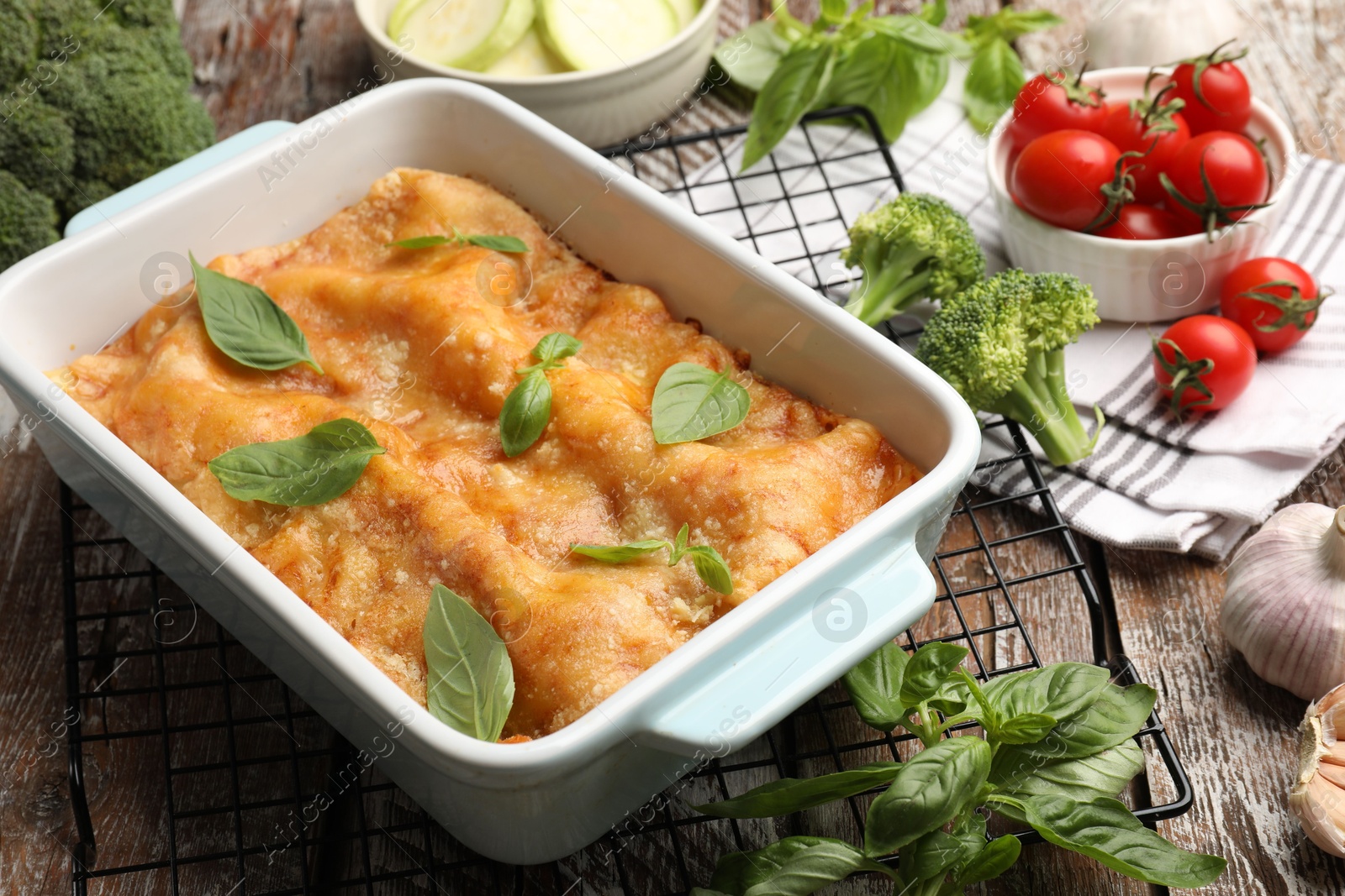 Photo of Tasty vegetarian lasagna in baking dish and ingredients on wooden table, closeup