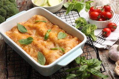 Photo of Tasty vegetarian lasagna in baking dish and ingredients on wooden table, closeup