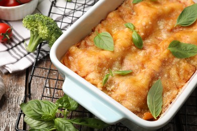 Photo of Tasty vegetarian lasagna in baking dish and ingredients on wooden table, closeup