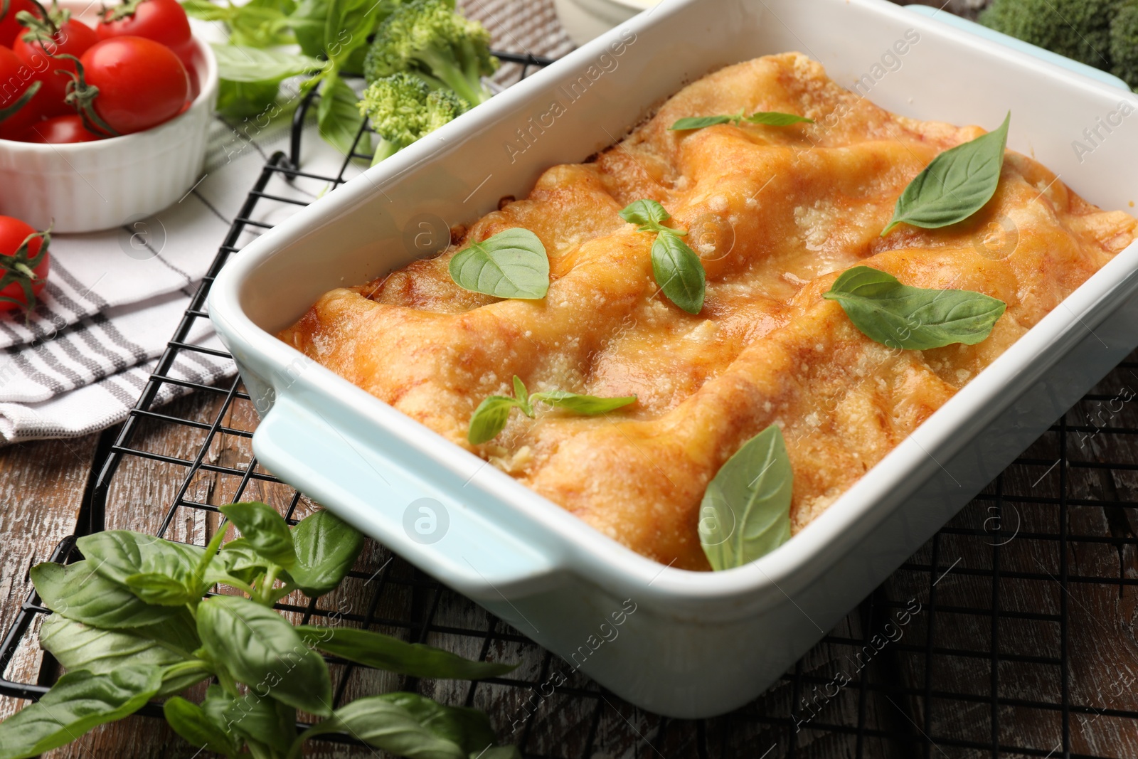 Photo of Tasty vegetarian lasagna in baking dish and ingredients on wooden table, closeup