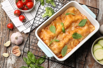 Photo of Tasty vegetarian lasagna in baking dish and ingredients on wooden table, flat lay
