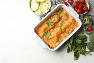 Photo of Tasty vegetarian lasagna in baking dish and ingredients on white table, flat lay. Space for text