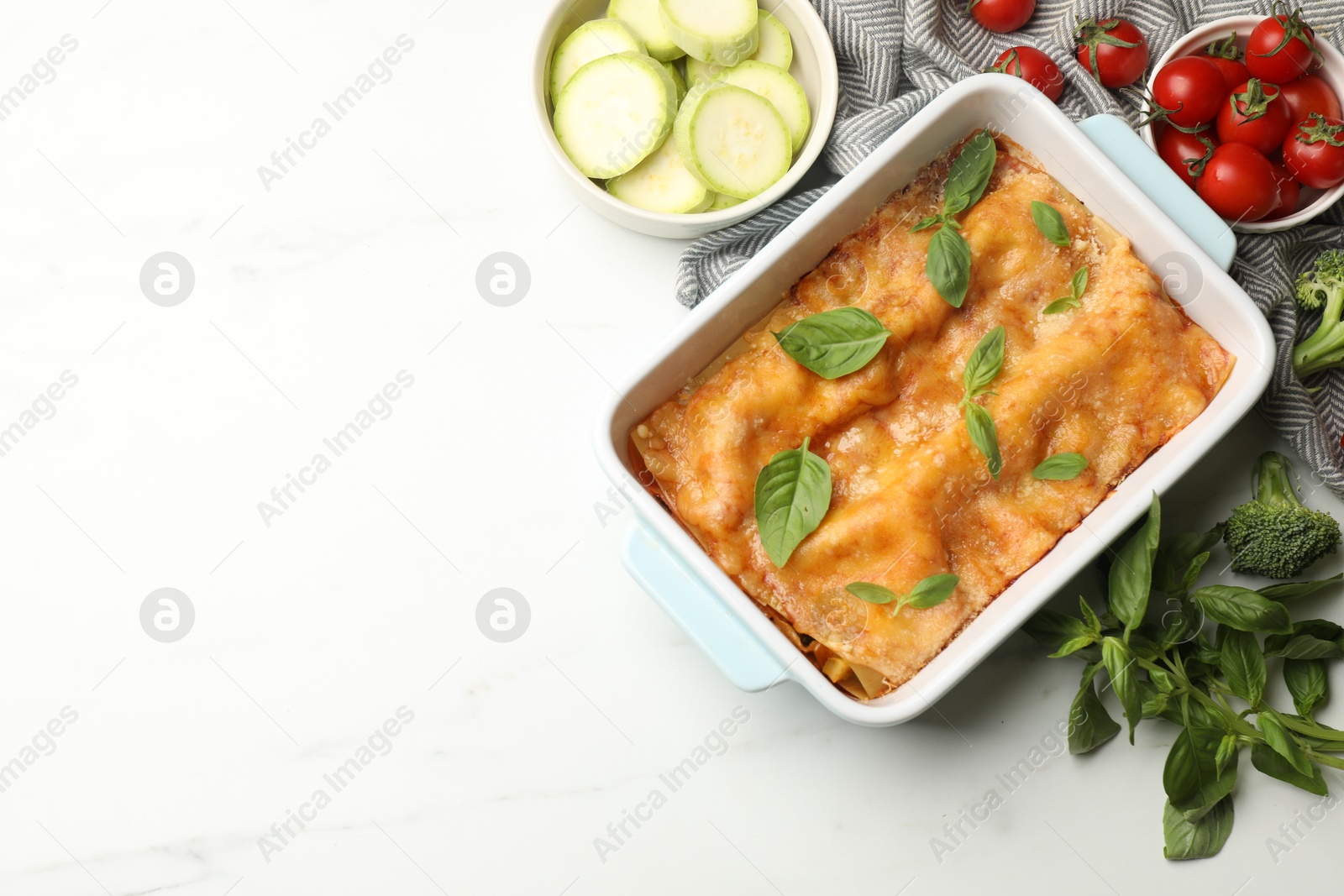 Tasty vegetarian lasagna in baking dish and ingredients on white table, flat lay. Space for text Photo of Tasty vegetarian lasagna in baking dish and ingredients on white table, flat lay. Space for text