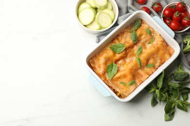 Photo of Tasty vegetarian lasagna in baking dish and ingredients on white table, flat lay. Space for text
