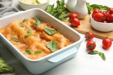 Photo of Tasty vegetarian lasagna in baking dish and ingredients on white table, closeup